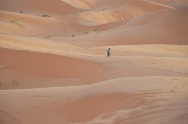 Sunset time at Merzouga with a berber man walking back to his tent. Merzouga is a small Moroccan town in the Sahara Desert, near the Algerian border.