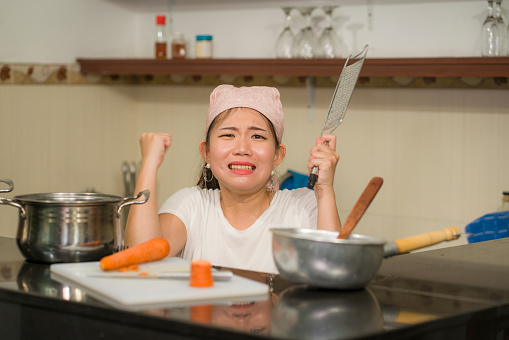lifestyle home portrait of beautiful overwhelmed and stressed Korean girl working in kitchen unhappy and upset housekeeping - young frustrated Asian woman screaming in domestic chores stress