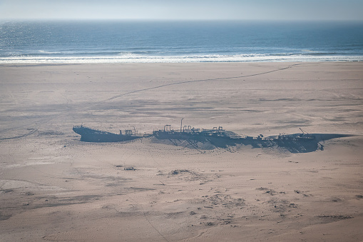 Abandoned old historic shipwreck covered from sand dunes in the skeleton coast desert at the border to the Atlantic Ocean. Aerial View, shot from Cessna flyover along the Namibian Skeleton Coast Desert, Nambia, South West Africa, Africa