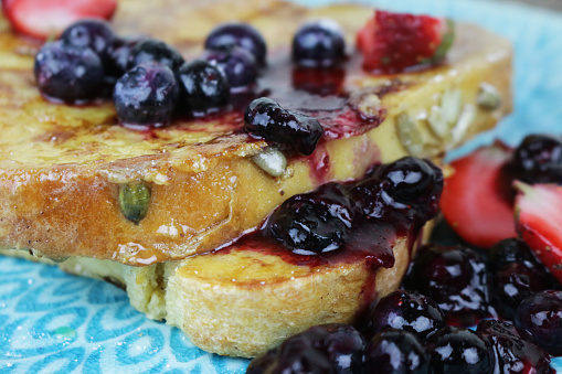 Stock photo of homemade eggy bread often called French toast on patterned, turquoise plate. This breakfast has been served with strawberries and blueberries and sprinkled with granulated sugar and fruit juice.