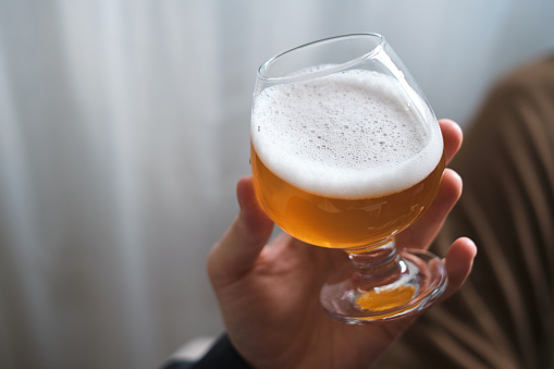 A glass of beer in the hands of a man. Tasting brewed craft beer. Lager beer with beautiful foam. Cold refreshment beverage. Alcohol drink from pub. Relaxation and enjoyment on beer degustation