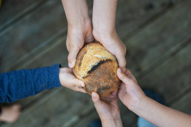 Hands of a family holding bread bun in a conceptual image of poverty and hunger.