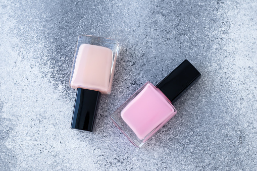 Two glass bottles of nail polish. Neutral beige and pink enamel on gray grunge concrete background. Top view. Beauty product for french manicure