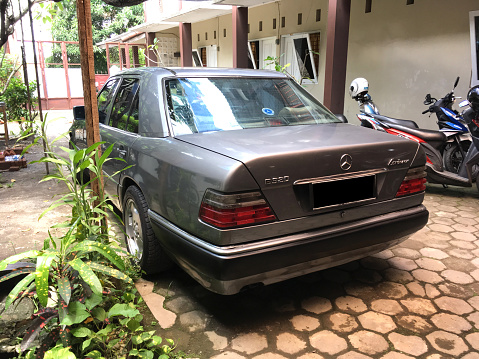 Yogyakarta, Indonesia - April 3, 2019: Mercedes Benz Classic W124-1990 series (Boxer) with 2300cc engine back view with silver color parked on the curb of a building in Yogyakarta, Indonesia