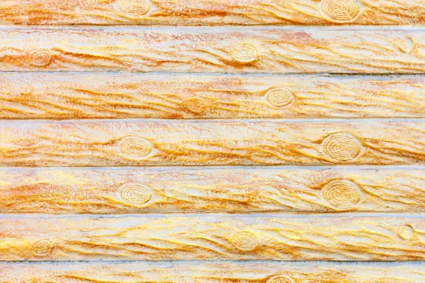 The texture and background of the concrete wall under a stylized wooden fence in the form of horizontal logs in yellow-gold color.