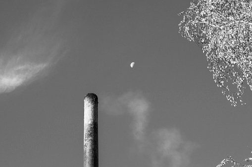 smoke from a steel pipe against a blue sky with the moon