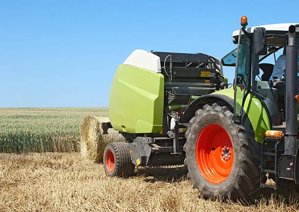 Tractor with round baler on the field after crop
