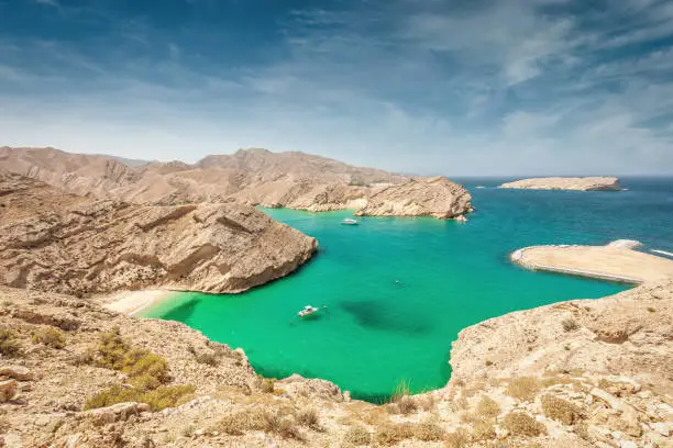 Beautiful green, blue lagoon with a small hidden beach between the harsh rocky coastal landscape at the Gulf of Oman Rocky Coast. Sultanate of Oman, Middle East