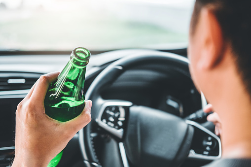 Drunk man driving a car on the road holding bottle beer Dangerous drunk driving concept