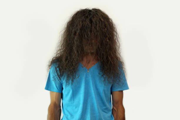 poses in studio against white background. Cut bangs. retrato de hombre elegante con el pelo largo rizado desaliñado durante la cuarentena de la corona covid-19 infección necesita un corte de pelo. cuidado de peluquería y peluquería. cabello dañado, necesita tratamiento. desacuerdo y expresiones negativa