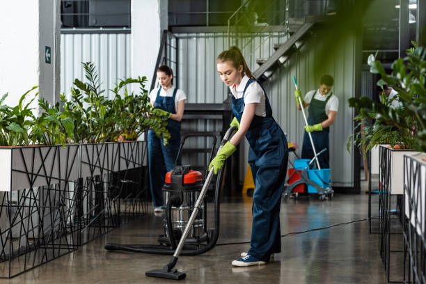 молодой уборщик пылесосить пол в офисе рядом с коллегами - cleaner стоковые фото и изображения