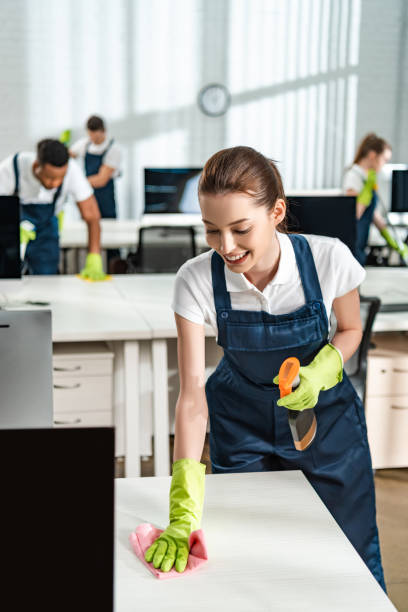 istock cheerful cleaner in overalls cleaning office desk with rag 1222545485