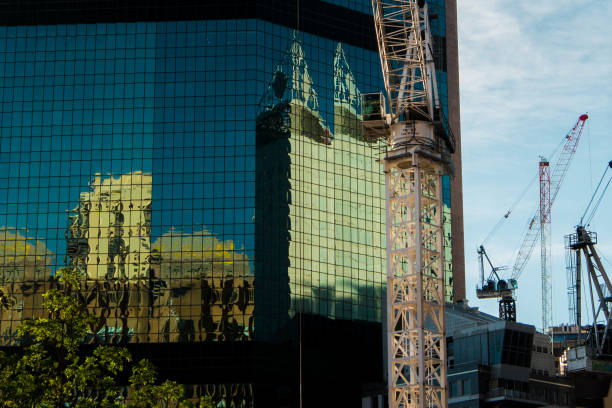 There are many construction sites viewed in the city with cranes everywhere. Reflections seen on the side of the skyscraper.