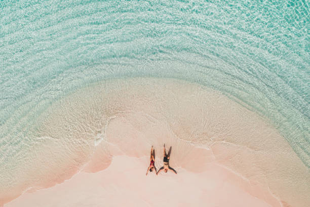 paar liegt am berühmten rosa strand im komodo nationalpark. türkis mint farbe klares wasser, tropischen urlaub auf flitterwochen. drohnen-luftaufnahme von oben. - tropical climate water leisure activity holidays stock-fotos und bilder