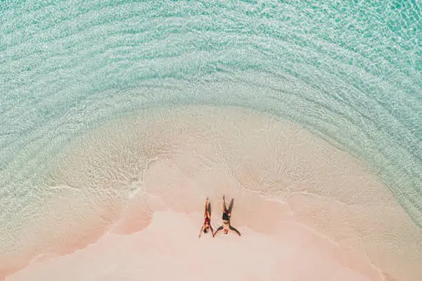Photo of Couple lying on famous pink beach in Komodo national park. Turquoise mint color clear water, tropical vacations on honeymoon. Drone aerial view from above.