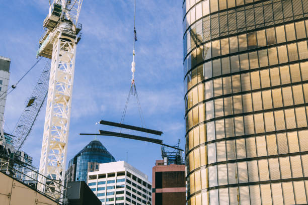 Crane in action in the city. Building materials being hoisted up to a building site with city corporate buildings in the background. The crane forms a shadow on the nearby gold coloured building. winch cable stock pictures, royalty-free photos & images