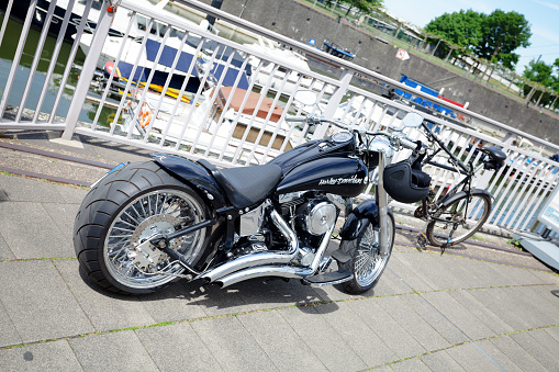 Black low seated Harley Davidson motorcycle with big exhausts standing and parked in Media Harbor Duesseldorf above yachts in background