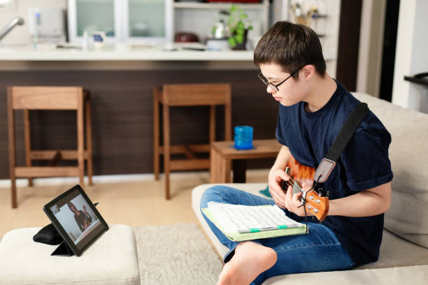 adolescent avec le syndrome de down' prenant des leçons de musique d’apprentissage à distance à la maison sur l’internet - guitar child music learning photos et images de collection