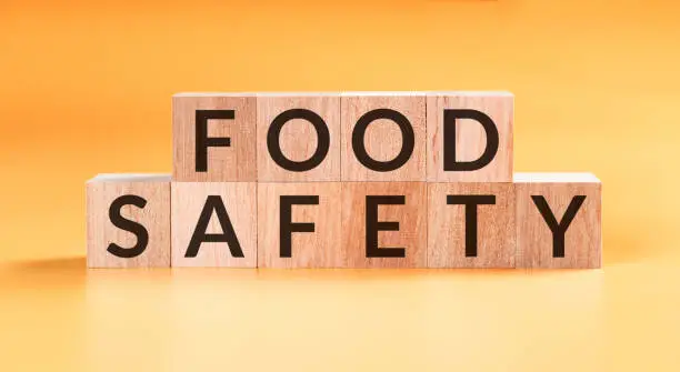 Photo of food safety word written on wood block on yellow background