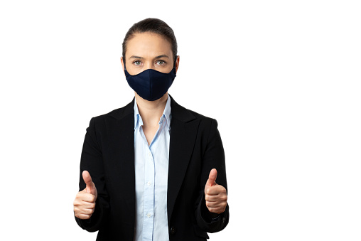 Caucasian female with protective face mask is looking at camera and is doing thumbs up gesture in front of pure white  background.