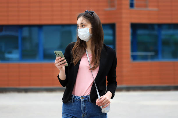istock Young woman wearing face-protective mask is using her smart phone 1222556577