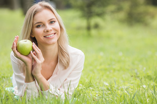 Woman with apple laying on green grass, background with copy space