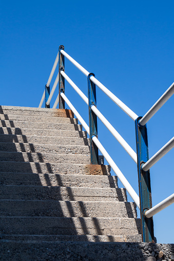 Simple concrete staircase outdoors with a diagonal shadow and a metal railing. Bright blue sky. Heraklion, Crete, Greece.