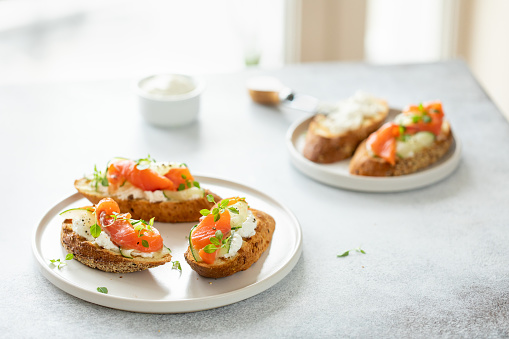 Bruschetta with salmon, curd cheese and cucumber on toast in high key style on white background.