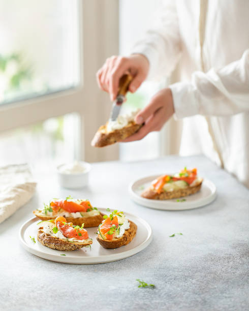 woman make bruschetta with salmon, curd cheese and cucumber on toast in high key style on white background. - bruschetta buffet party food imagens e fotografias de stock