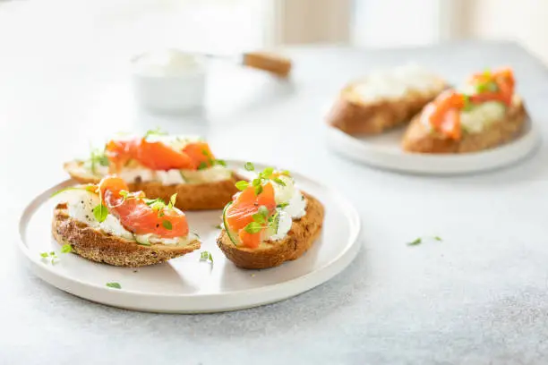 Photo of Bruschetta with salmon, curd cheese and cucumber on toast in high key style on white background.