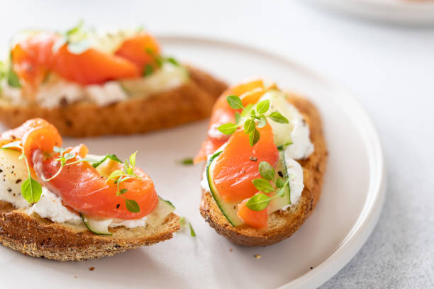 Bruschetta with salmon, curd cheese and cucumber on toast in high key style on white background. Bruschetta with salmon, curd cheese and cucumber on toast in high key style on white background. crostini stock pictures, royalty-free photos & images