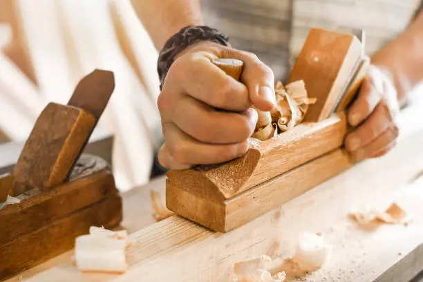 The carpenters using old spokeshave or plane to decorate the woodboard.