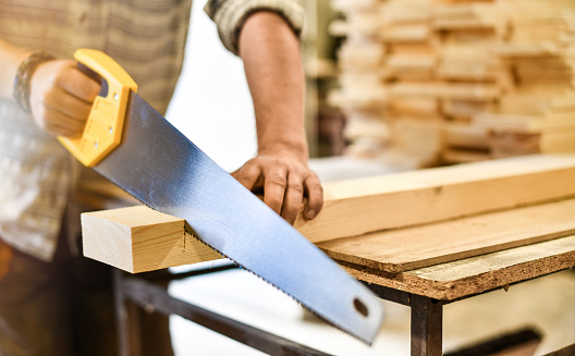 Worker hands use a wood cutter or saw on wooden board.