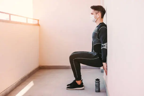 Photo of Sports man in face mask doing leg exercises at home