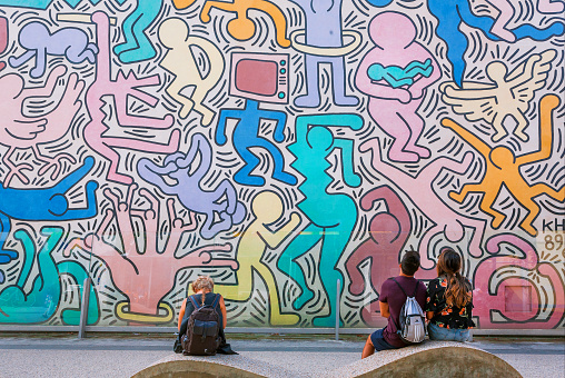 Pisa, Italy: People look at wall with artwork by modern artist Keith Haring, famous in pop-art style on 19 September 2018. American artist Keith Haring, popular street art figure, died in 1990.