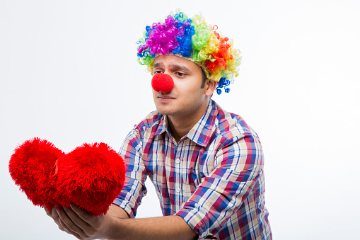Male clown kissing female clown. Clowns with face painted wearing colorful costumes and wigs, white background.