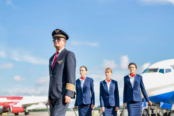 portrait of mature pilot walking with three young beautiful flight attendants against airplane in airport - cabin crew pilot airport walking imagens e fotografias de stock