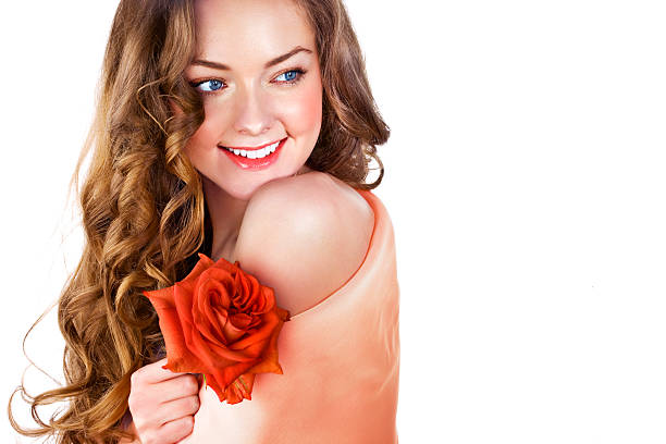 Woman holding roses close to her face looking into the camera with a smile.