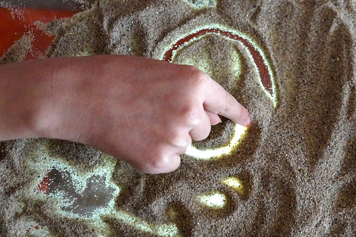Children's hand draws on a glass transparent table with sand backlighting, sand therapy