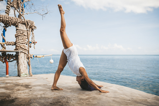 Young woman doing yoga at the beach on the cliff