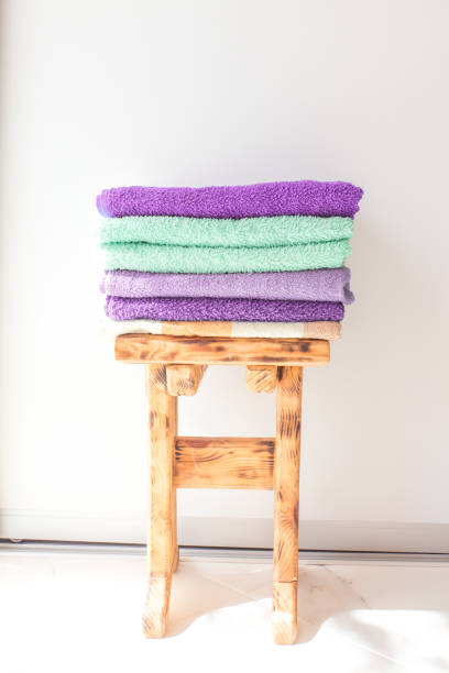 istock stack of bright cotton towels on a wooden stool. White wall. Mock up for text. Minimal concept. Card with copy space 1222589001