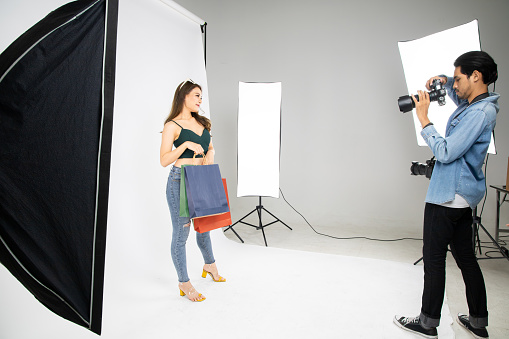 Model beautiful girl posing for a photo taken with a professional photographer in the studio in shopping concept. Photographer and model. Young man photographing fashion model.
