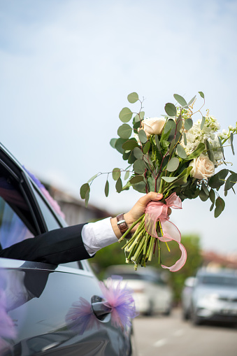 Bridegroom holding flower bouquet out from his wedding car