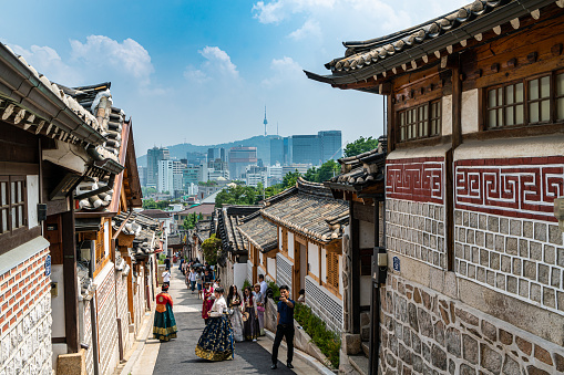 Seoul, South Korea - June 29, 2018:  Tourists dressing in traditional Korean Hanbok while walking in historic Korean style neighborhood in Bukchon Hanok village in Seoul, South Korea.