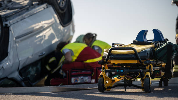 paramédicos y bomberos llegan a la escena del accidente de tráfico. profesionales rescatan a la víctima herida atrapada en el vehículo rollover extricando, dando primeros auxilios y extinguiendo el fuego - action fire department car men fotografías e imágenes de stock