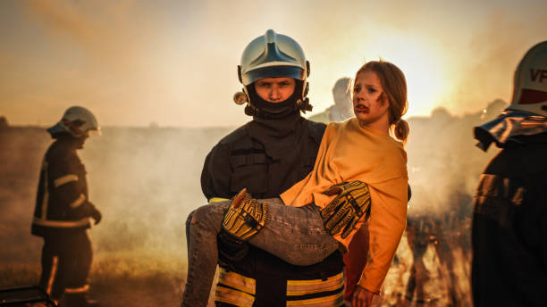 용감한 소방관은 부상당한 어린 소녀를 안전하게 데려다 주었습니다. 용감한 구급대원과 소방관과 배경 자동차 충돌 교통 사고에서 생명을 구하고 화재와 싸우십시오. - fire department heroes portrait occupation 뉴스 사진 이미지