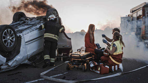 accident de la route : les ambulanciers paramédicaux et les pompiers sauvent des victimes blessées. les médecins donnent les premiers soins à une passagère. les pompiers utilisent l’épandeur de cutters hydrauliques pour ouvrir le véhicule - car road highway open photos et images de collection