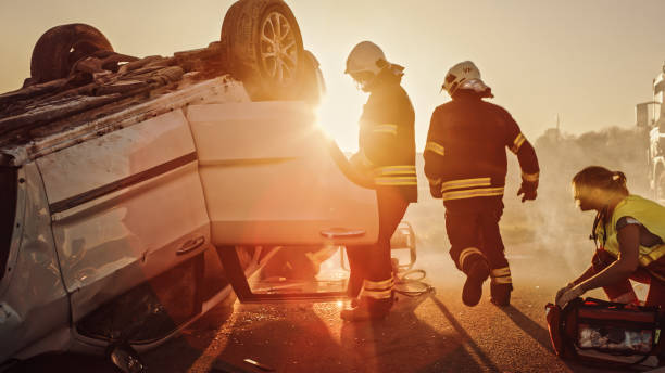 istock Car Crash Traffic Accident: Paramedics and Firefighters Plan Rescuing Passengers Trapped in Rollover Vehicle. Medics Prepare Stretchers and First Aid Equipment. Firemen Use Hydraulic Cutters Spreader 1222597715