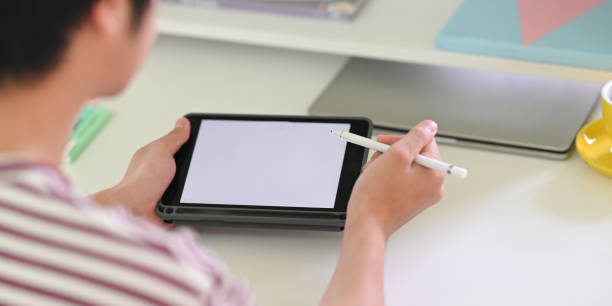 istock Behind shot of young creative man drawing on white blank screen computer tablet by stylus pen while sitting at the white working desk over modern working studio as background. 1222599203
