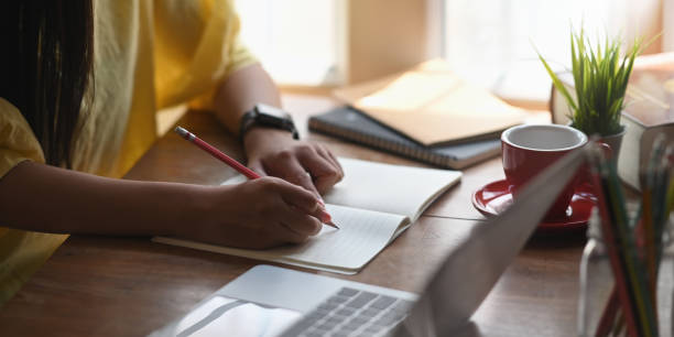 istock Cropped image of woman writing on notebook that putting on working desk and surrounded by computer laptop and notebook over comfortable living room as background. 1222599211